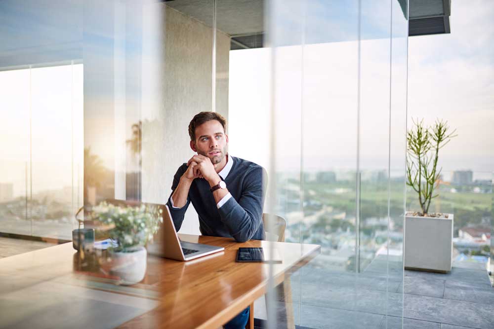 man at laptop looking outside window 