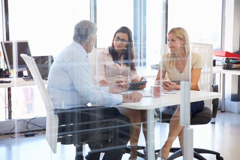 image of two women and a man sitting around a desk in an office
